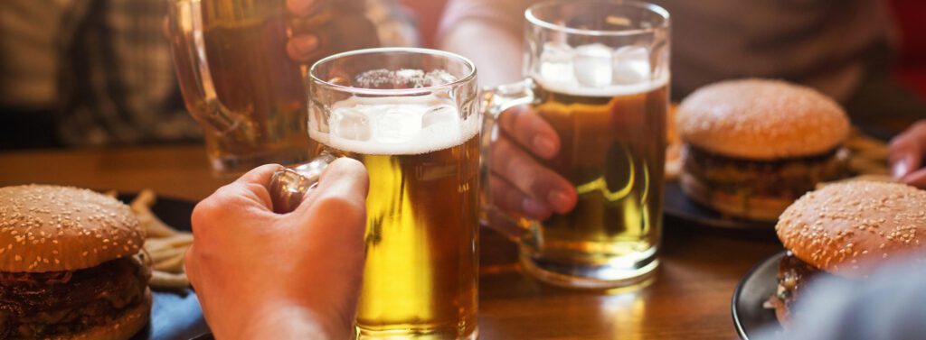 Two people holding mugs of beer and enjoying burgers and french fries